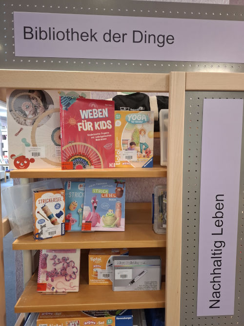 Bibliothek der Dinge in der Eichenauer Gemeindebücherei Zu sehen ist ein Regal, in dem verschiedene Gegenstände, die zum Verleih angeboten werden, ausgestellt sind, z.B. eine Strickliesel, ein Lautsprecher oder ein Polierstift