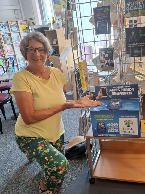Sabine Canditt präsentiert die neue Sammelbox in der Bücherei Zu sehen ist Sabine Canditt neben einer Handy-Sammelbox der Deutschen Umwelthilfe