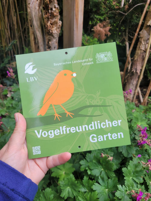 Eine Hand, die ein Schild mit der Aufschrift »Vogelfreundlicher Garten« hält